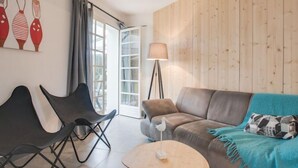 A modern living room with a sofa, two chairs, a small round table, a floor lamp, and a large window with curtains.
