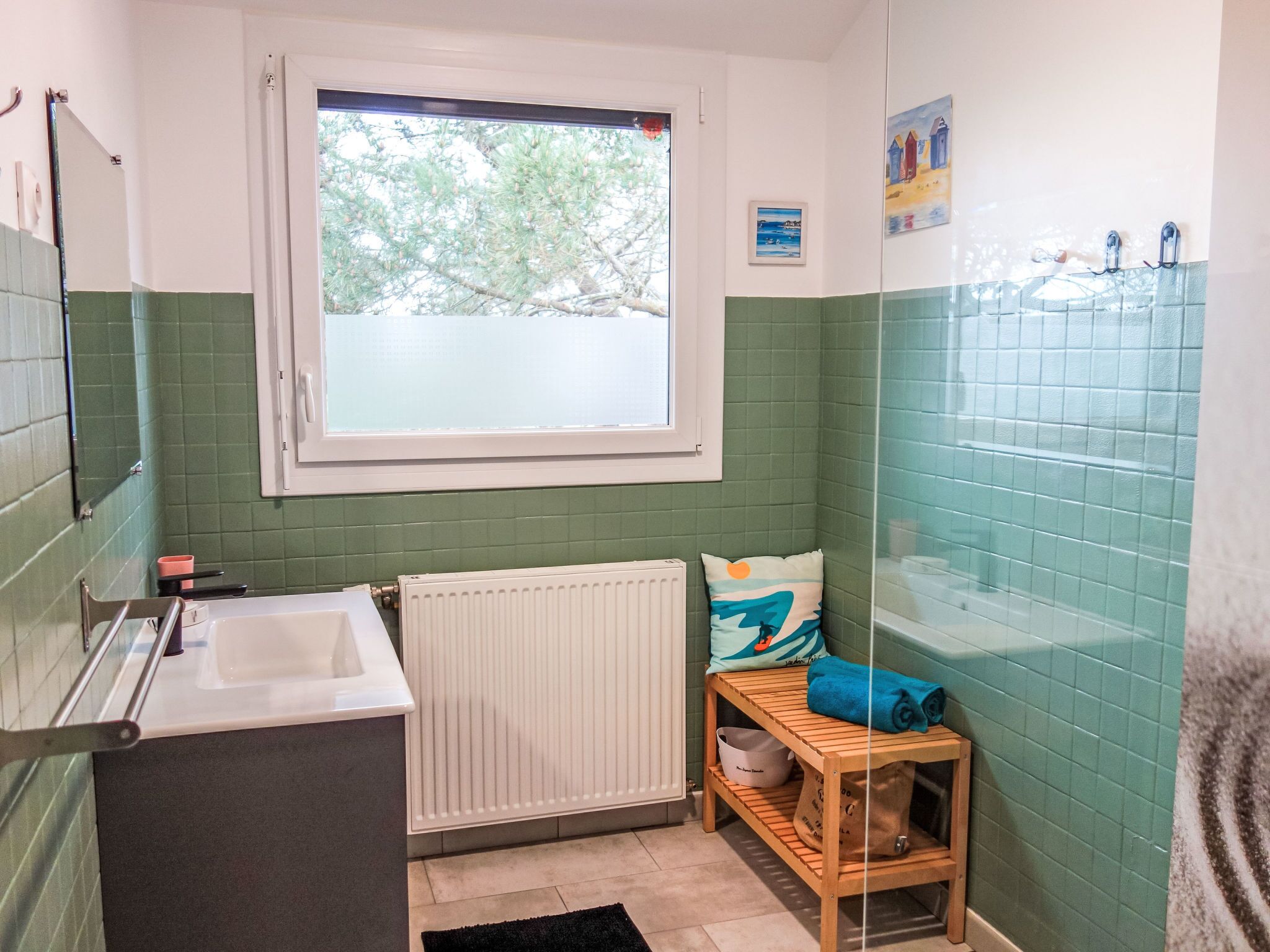 A small bathroom with a window, a radiator, a sink, and a wooden shelf with towels.
