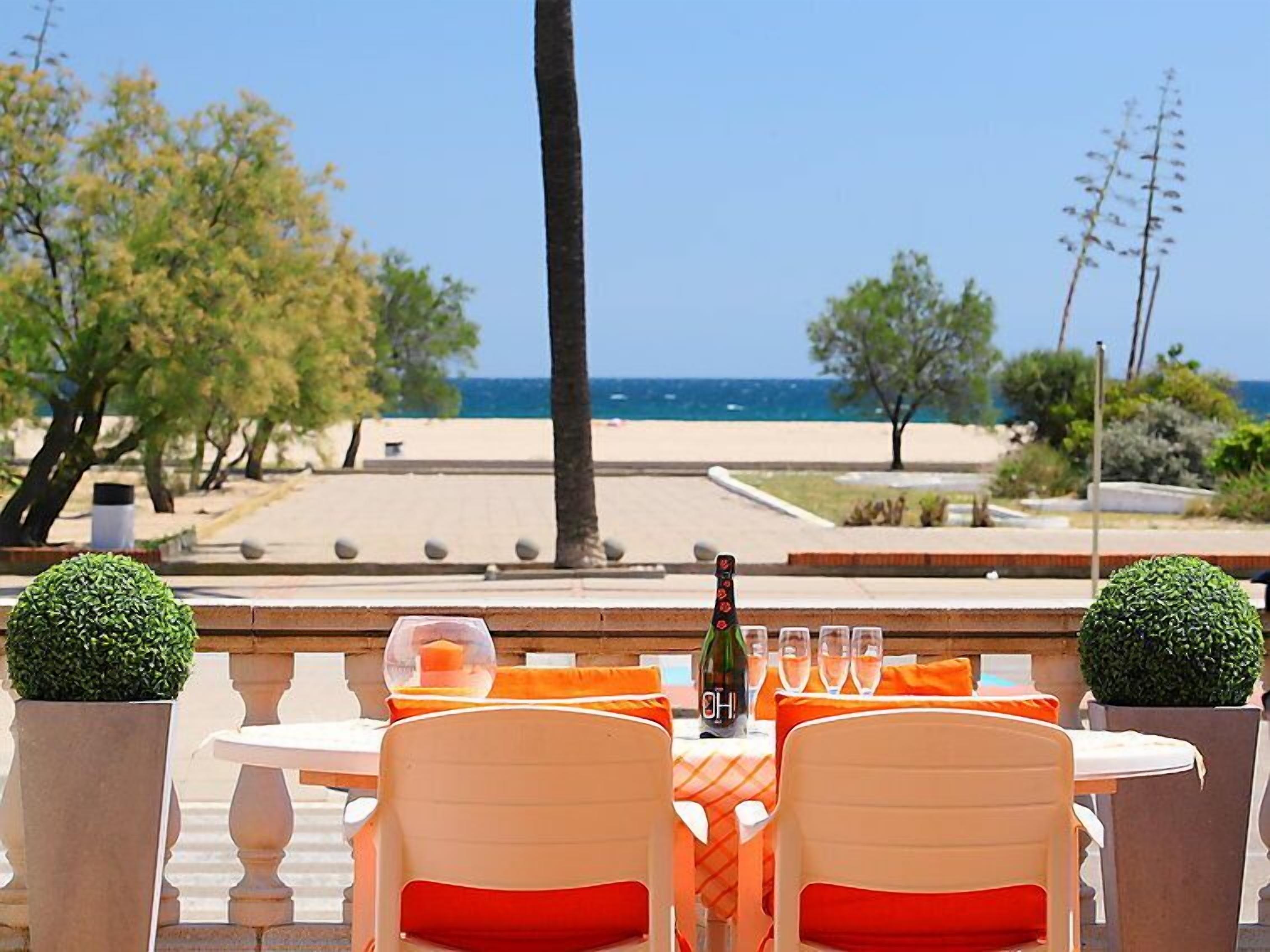 Een terras met uitzicht op het strand, tafels met oranje kussens en een fles wijn op tafel.