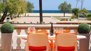 Un área de comedor al aire libre con vista a la playa, mesas con cojines naranja y una botella de vino sobre la mesa.