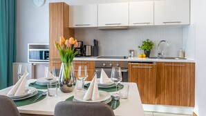 Eine moderne Küche mit weißen Schränken, einer Spüle und einem Herd. Ein Esstisch ist gedeckt mit Tellern, Gläsern und einem Blumenstrauß.