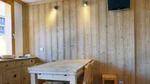 A wooden-paneled room with a table and chairs, a television mounted on the wall, and a window with a view of a building outside. - 10m from ski slopes, 1st floor, balcony, 27m², Méribel-Mottaret (Méribel - Les Allues)