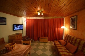 Una habitación acogedora con techo de madera, televisión, sofá, sillón, mesa y lámpara.