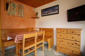 A cozy room with a wooden bed, a small table with a checkered tablecloth, a wooden dresser, and a wall-mounted TV.