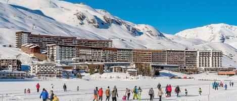 A ski resort with multiple buildings, including a large hotel with multiple floors and balconies, surrounded by snow-covered mountains.
