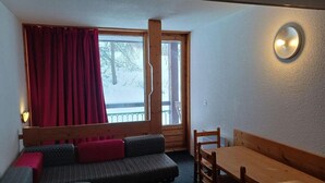 A cozy room with a sofa, a wooden table, and a window with curtains. - 50m from resort center, 8th floor, view mountain, balcony, tv, 42m², Les Arcs (Les Arcs)