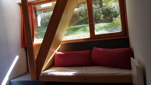 A small, cozy room with a slanted ceiling, a bed with red pillows, and a window overlooking a garden. - 50m from resort center, 8th floor, view mountain, balcony, tv, 42m², Les Arcs (Les Arcs)