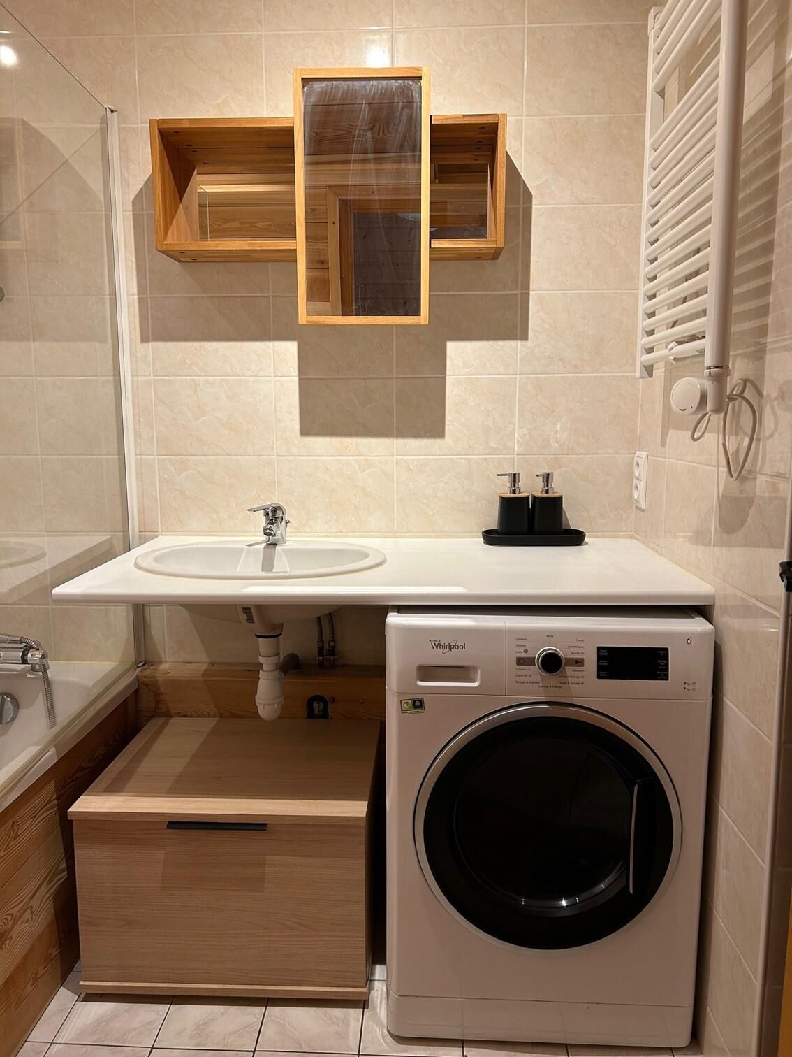 A compact bathroom with a sink, mirror, and a built-in washing machine.
