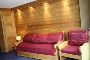 A wooden cabin room with a bed, two chairs, a nightstand, and a lamp.