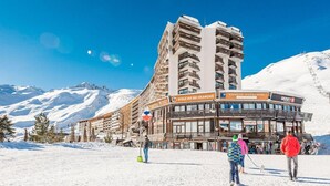 Een gebouw van een skigebied met meerdere balkons en borden met 'Ecole du Ski Francais' en 'Banque Populaire'.