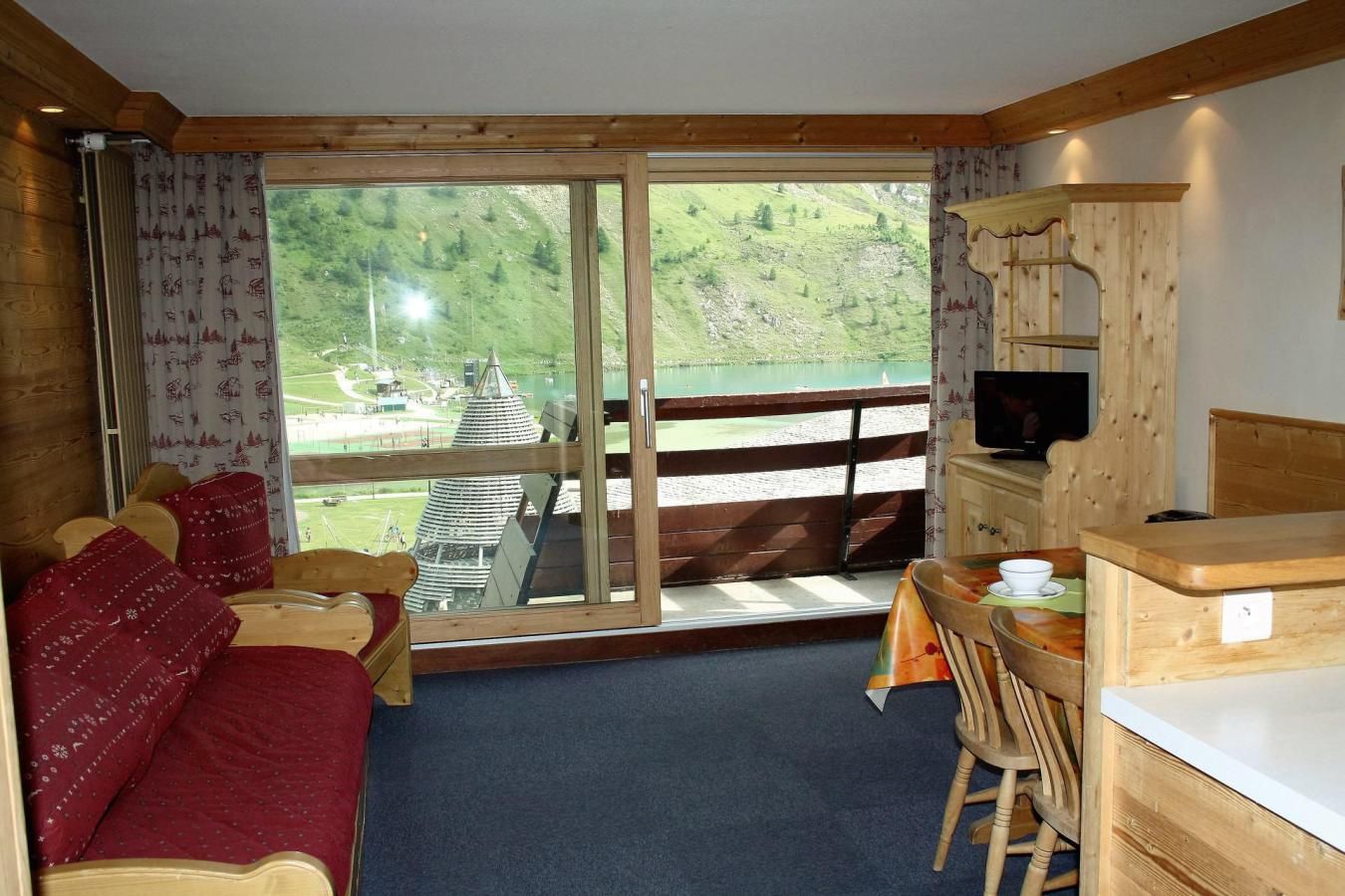 A room with a bed, a desk, a chair, a television, and a view of a lake and mountains.