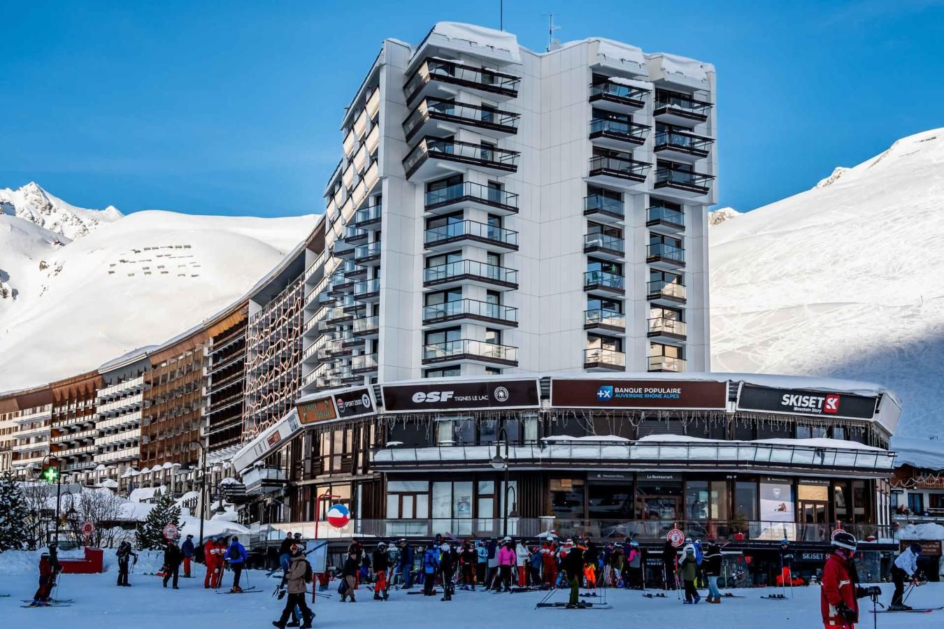 A modern hotel with multiple floors, ski shops, and a ski resort in the background.