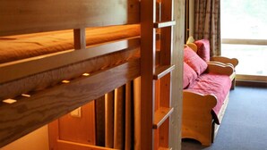 Een slaapkamer met stapelbed, houten hoofdbord, raam met gordijnen en bed met roze beddengoed.