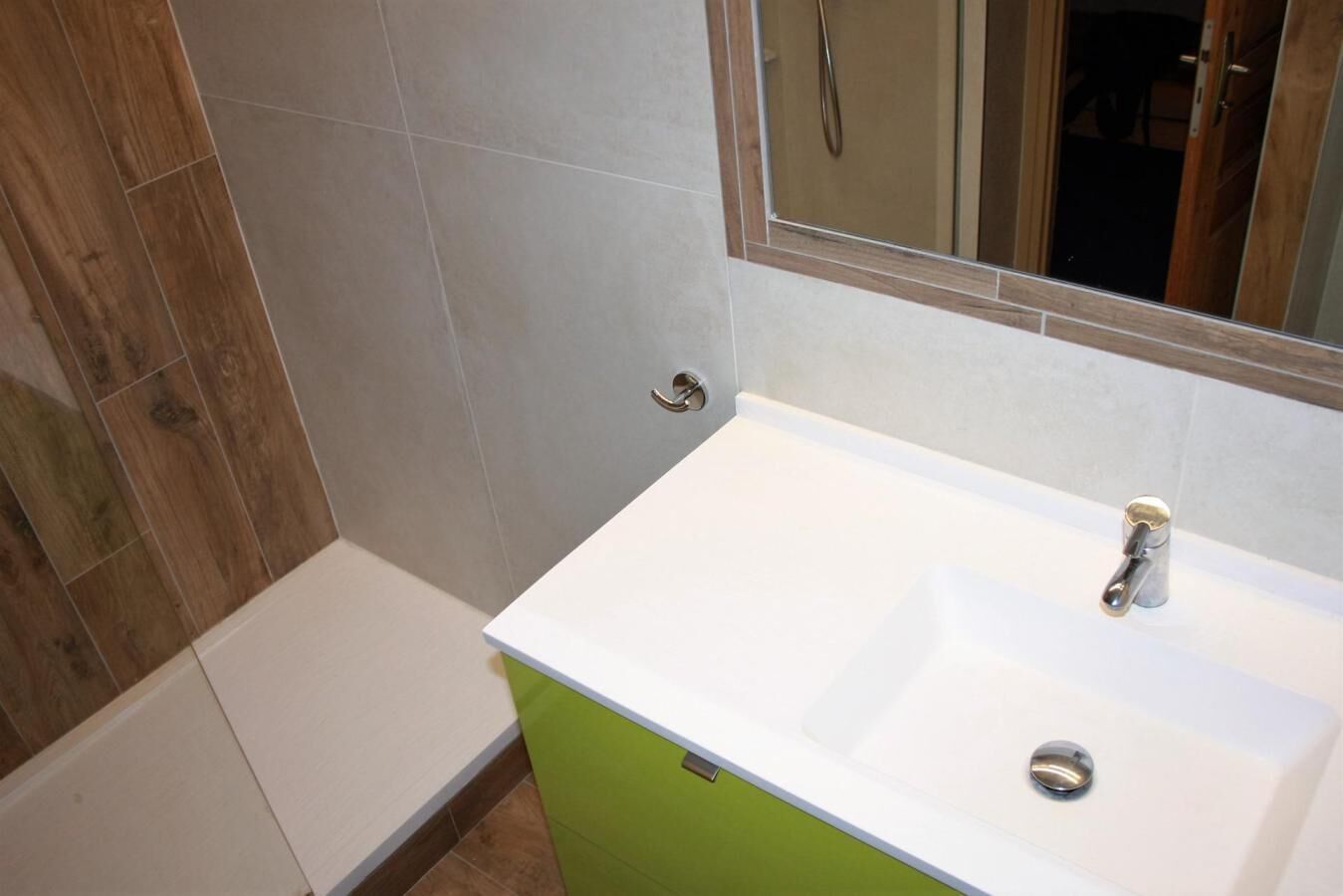 A bathroom with a white sink, green cabinet, and a mirror above it.