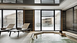 A modern indoor swimming pool with a view of a building through large windows. - Wifi, 200m from shops, fitness, swimming pool, sauna, hammam, balcony, tv, ski locker, 60m², Samoëns (Samoëns)