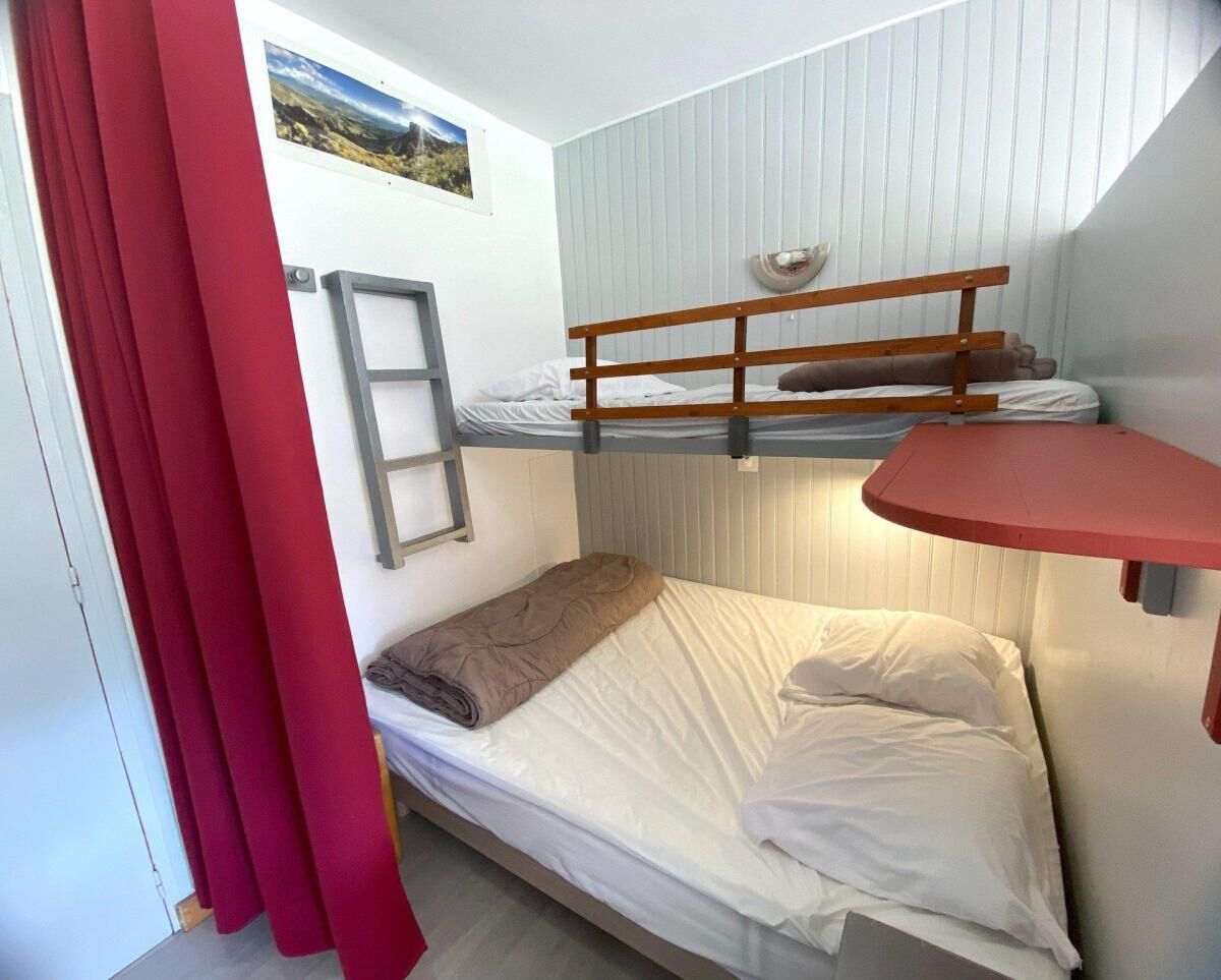 Ein kleines Zimmer mit Etagenbett, Schreibtisch und einer Stehleiter.