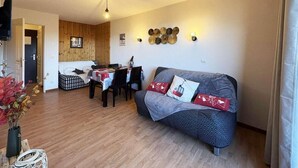 Un salon chaleureux avec un canapé, une table à manger et des chaises, et un coin cuisine à l’arrière-plan.