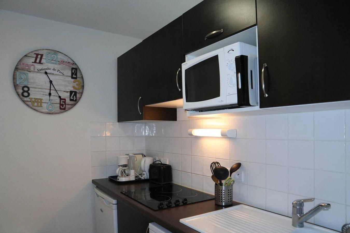 Una cocina con microondas, cafetera y un reloj en la pared.