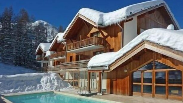 Un chalet doté d’une piscine, d’une façade en bois, de balcons et surplombant un paysage enneigé.