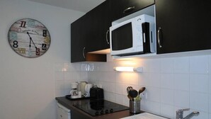 Une cuisine avec des meubles de couleur noire, un micro-ondes blanc, une machine à café et une horloge au mur.