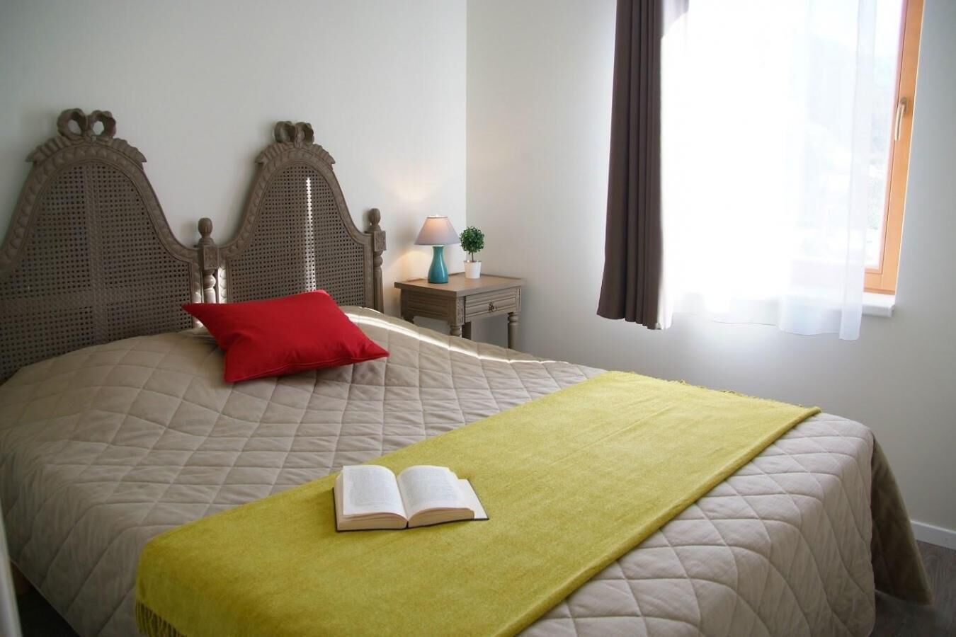 A neatly made bed with a red pillow, a green blanket, and an open book on the bed.