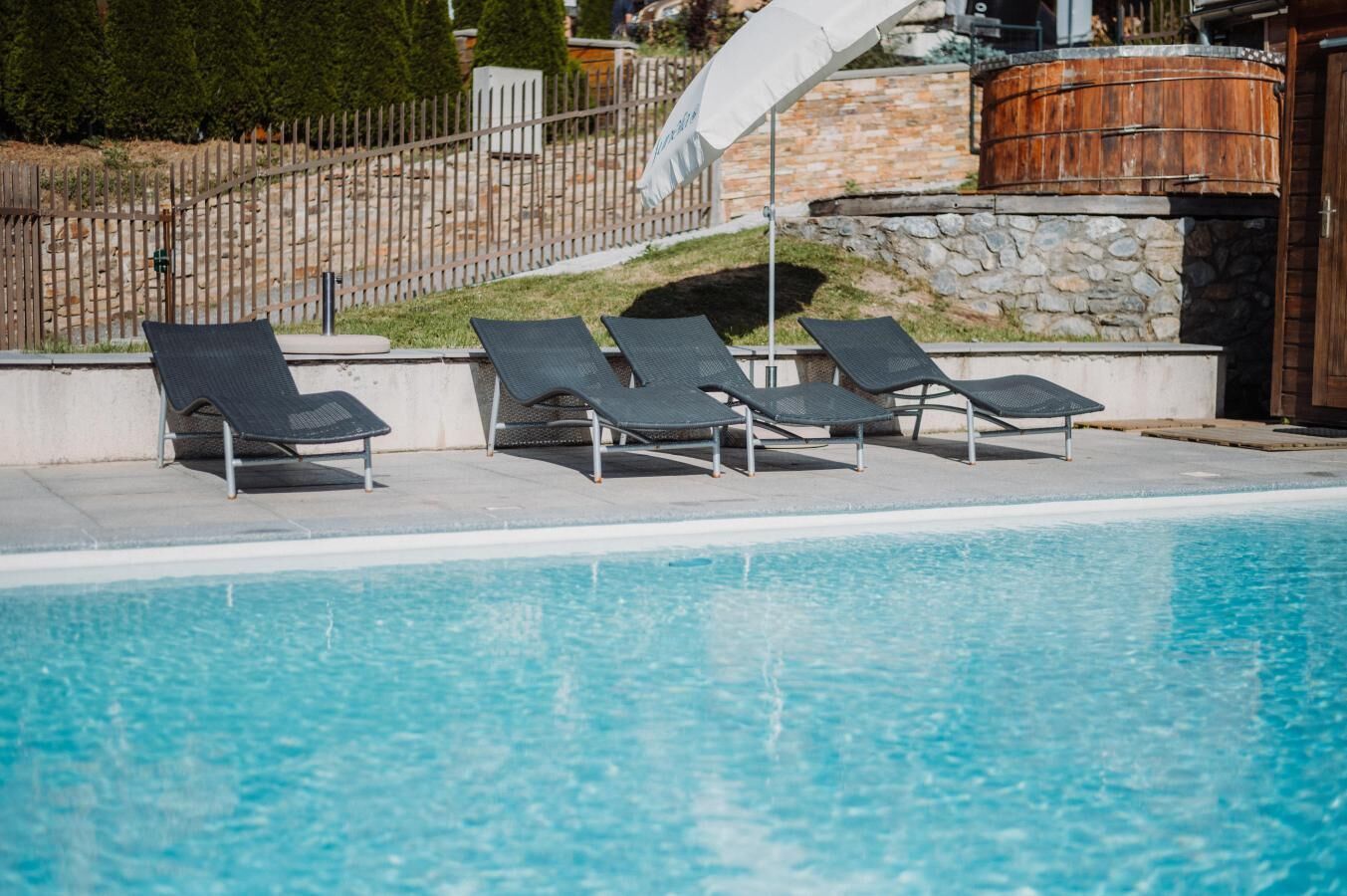 Ein Schwimmbecken mit vier Liegestühlen und einer Steinmauer im Hintergrund.