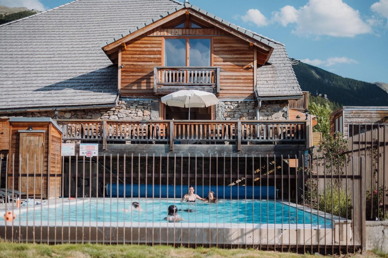 A wooden cabin with a balcony overlooking a swimming pool.