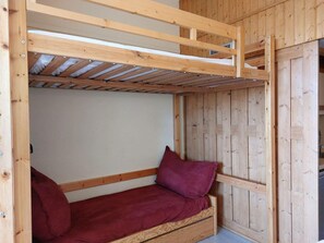 A wooden bunk bed with a red mattress and pillows, built into a cabin-style room with wooden walls and a sloped ceiling.