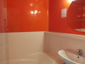 A bathroom with a white bathtub and sink, orange walls, and a mirror above the sink.