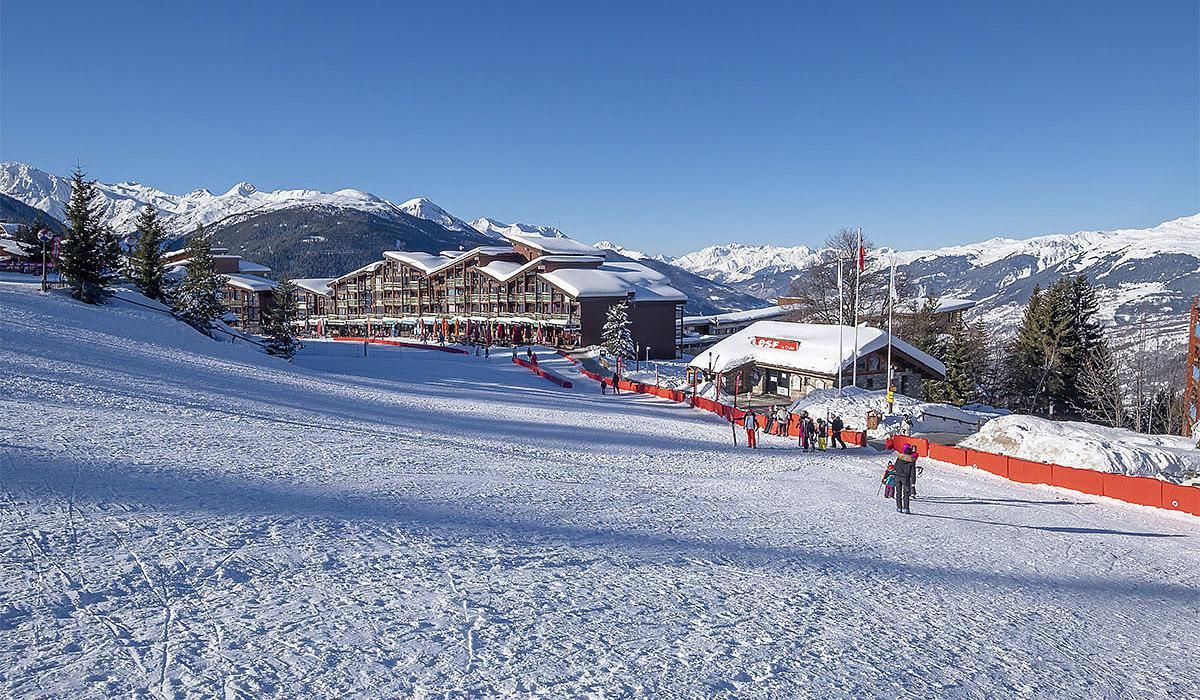 Estació d'esquí amb diverses cases rurals, una pista d'esquí i muntanyes nevades al fons.