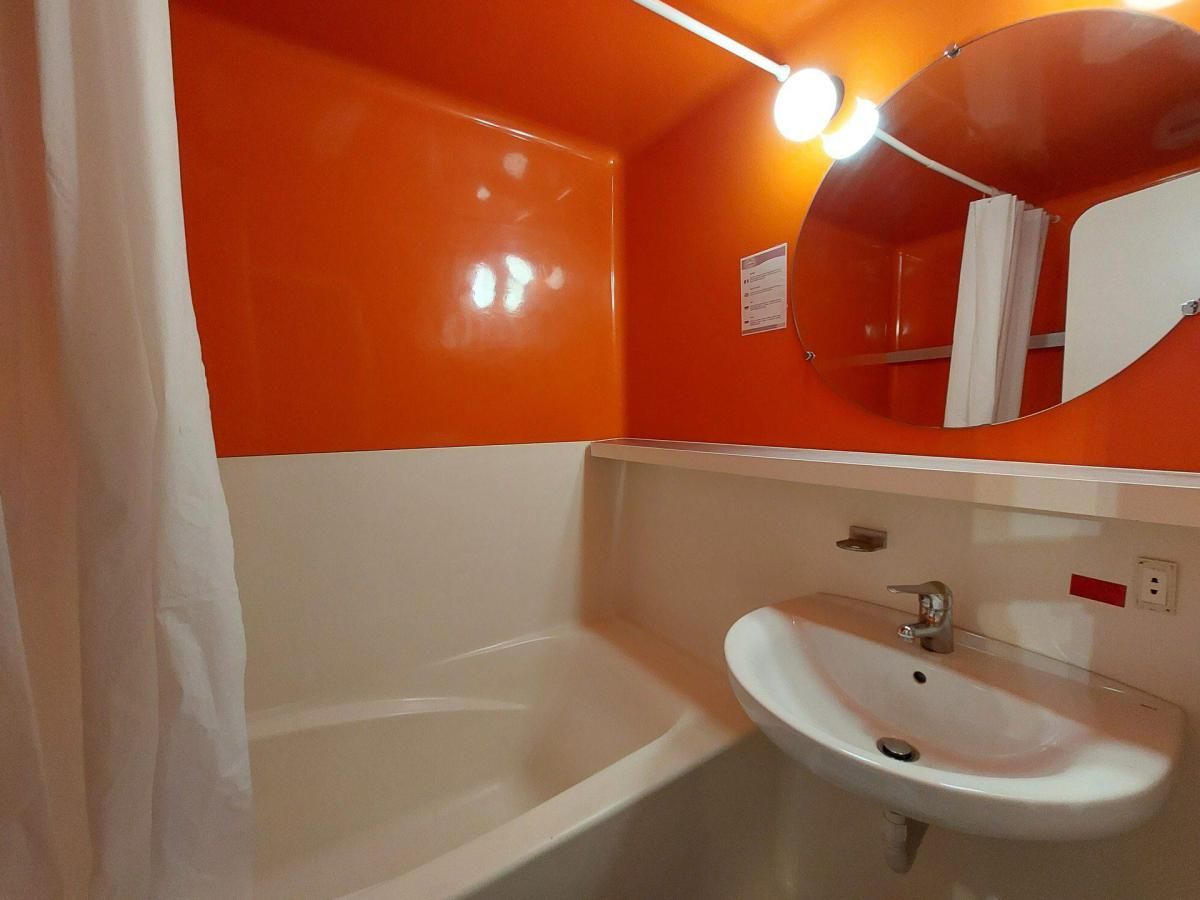 Un bagno con una vasca da bagno bianca, un lavandino bianco e una parete arancione.
