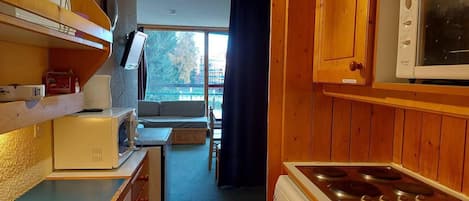 A compact kitchen with wooden cabinets, a microwave, a stove, and a small dining area with a table and chairs.
