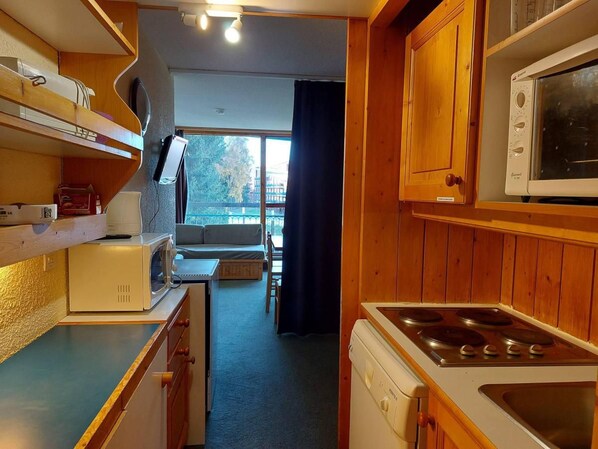 A compact kitchen with wooden cabinets, a microwave, a stove, and a small dining area with a table and chairs.