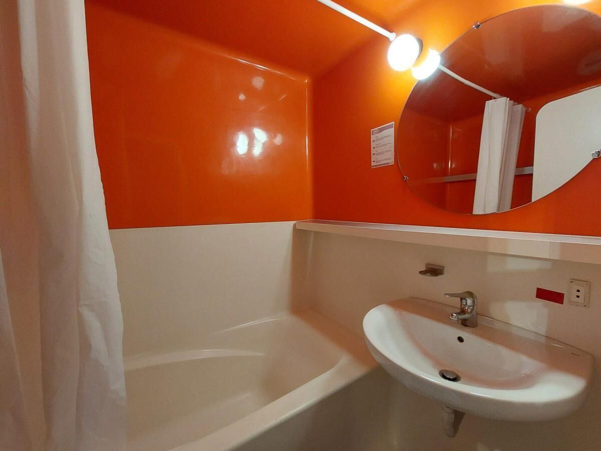 A bathroom with a white bathtub, a white sink, and an orange wall.