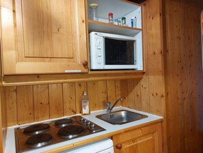 A compact kitchen with wooden cabinets, a microwave, a stove, and a sink.