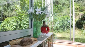 A kitchen counter with bread, a vase with flowers, and a window overlooking a garden.