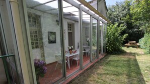 A covered patio with a table and chairs, a small garden area, and a wooden bench.