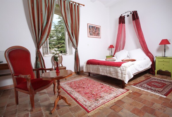 A bedroom with a bed, a chair, a table, and a window with curtains.