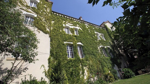 A building with multiple windows and a white facade partially covered by green ivy.