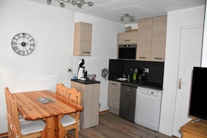 Cozinha compacta com mesa de jantar de madeira, cafeteira e máquina de lavar louça.