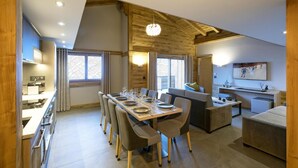 A modern interior with a dining area, kitchen, and living space, featuring wooden beams, large windows, and contemporary furnishings. - Wifi, fitness, swimming pool, sauna, hammam, balcony, tv, ski locker, 80m², Les Houches (Les Houches)