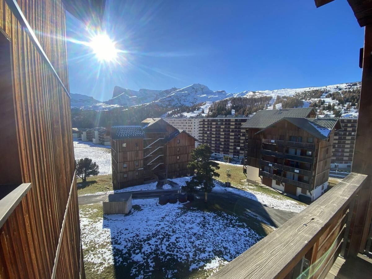 A view of a mountain resort with wooden buildings, a clear sky, and snow-covered ground.