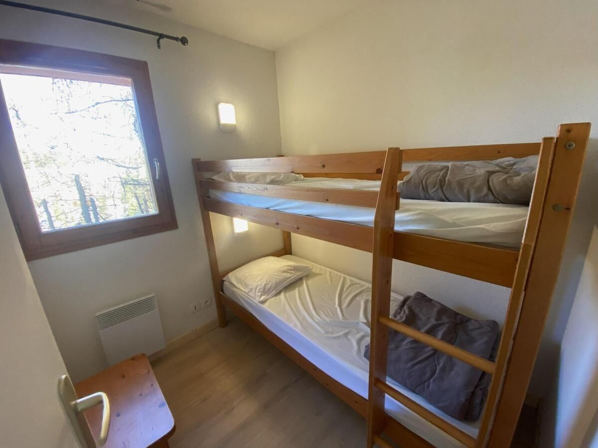 A bunk bed room with a window, a small table, and a wall-mounted light.