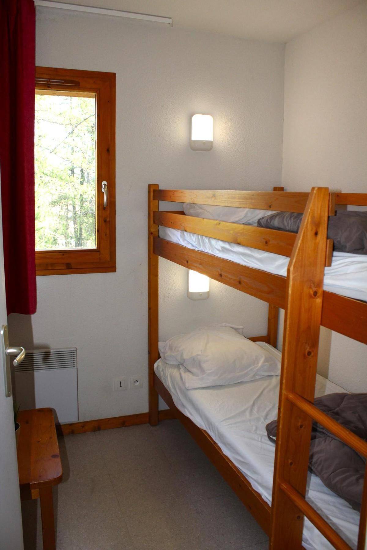 Une chambre avec un lit superposé, une fenêtre, un radiateur et une petite table.