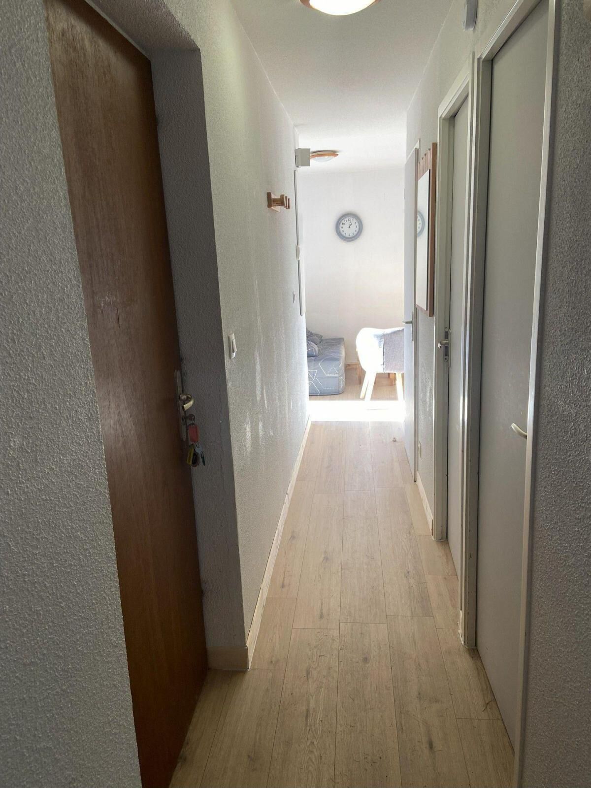 Ein Flur mit Holzboden, einer Uhr an der Wand und einer Tür links.