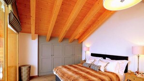 A bedroom with a wooden ceiling, a large bed with a fur throw, two bedside tables with lamps, and a grey wardrobe. - Chalet, 250m from ski slopes, balcony, fireplace or stove, parking, tv, 150m², Thyon (Hérémence)
