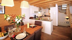 A modern kitchen with white cabinets, a central island, and a dining area with wooden furniture and a vase of flowers. - Chalet, 250m from ski slopes, balcony, fireplace or stove, parking, tv, 150m², Thyon (Hérémence)