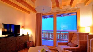 A cozy room with a television, a wooden cabinet, a cushioned bench, and a balcony with a railing. - Chalet, 250m from ski slopes, balcony, fireplace or stove, parking, tv, 150m², Thyon (Hérémence)