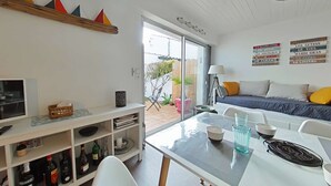 Una sala moderna con sofá, una mesa de comedor con sillas, televisor y estantería con diversos objetos.