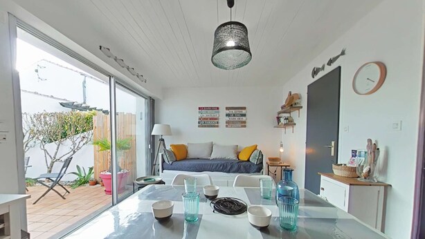 Una sala moderna con una mesa de comedor de vidrio, un sofá y una cama. Hay elementos decorativos en las paredes y una ventana con vistas al exterior.